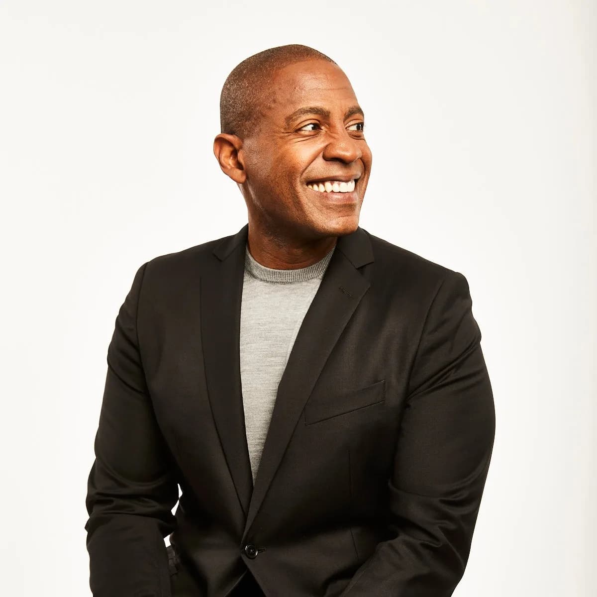 Carlos Watson smiling in a dark blazer